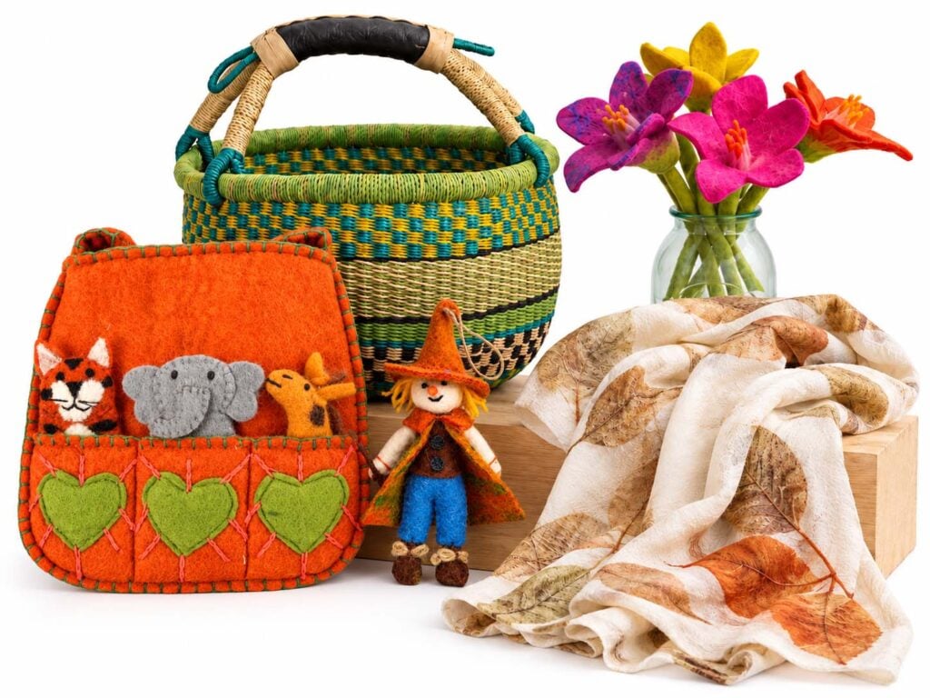 A woven basket, felt zoo finger puppet bag, merino and silk scarf, felt flowers and a scarecrow decoration arranged around a wooden block.